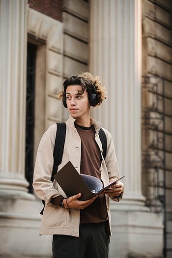 ذكر عرقي،  مبنى الجامعة،  مجلد عقد،  شاب،  سماعات الرأس،  تعبيرٌ مُتأمّل،  الإعداد في الهواء الطلق،  الحياة الطلابية،  البيئة الأكاديمية،  لباس غير رسمي،  حقيبة ظهر