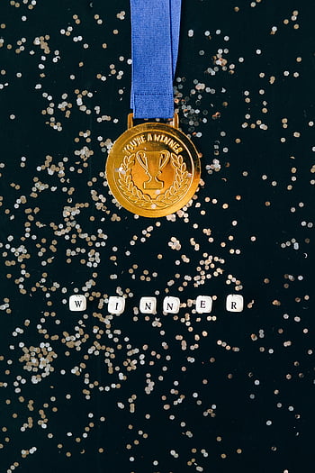 Zlatá medaile, černý povrch, konfety, vítěz, detailní záběr, oslava, cena, vítězství, úspěch, trofej, modrá stužka