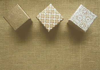 brown and white gift boxes, decorative gift boxes, textured burlap surface, warm rustic look, three gift boxes, burlap background, rustic gift boxes, gift box arrangement, brown gift boxes, white gift boxes, floral pattern boxes