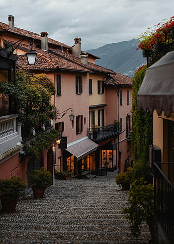 Passi pavimentati, strada della città vecchia, tramonto, pittoresca strada europea, Case caratteristiche, Passi di ciottoli, crepuscolo, architettura europea, sfondo di montagna, lanterne di strada, piante in vaso