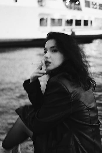 monochrome portrait, woman smoking, cigarette, black and white, young woman, sitting by river, artistic photography, outdoor portrait, urban scene, contemplative mood, fashion style