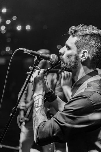 man playing flute, monochrome image, male musician, concert, black and white, tattooed arm, microphone, stage performance, musical performance, live music, flute player