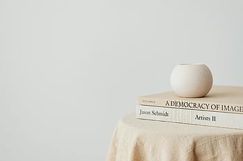 книги на масата, бяла стена, минималистичен дизайн, малка ваза, елегантен състав, проста композиция, декор за маса, бяла ваза, книжен стек, чист фон, Модерна естетика