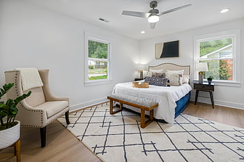 contemporary bedroom, stylish furniture, natural light, serene decor, white and brown bed, white wooden framed glass window, wooden floor, geometric rug, beige armchair, indoor plant, ceiling fan