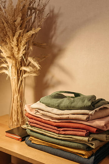 stacked clothes, folded clothes, wooden table, dried flowers, aesthetic arrangement, linen clothes, home decor, interior design, cozy atmosphere, natural elements, soft lighting