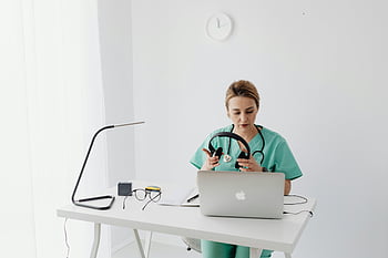 female doctor, scrubs, telehealth consultation, modern office, headphones, laptop, medical professional, healthcare worker, remote consultation, medical setting, telemedicine