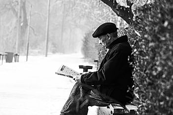 man sitting on bench, senior man, reading newspaper, snowy bench, tranquil winter park, winter scene, outdoor reading, elderly man, peaceful setting, black and white photo, winter park