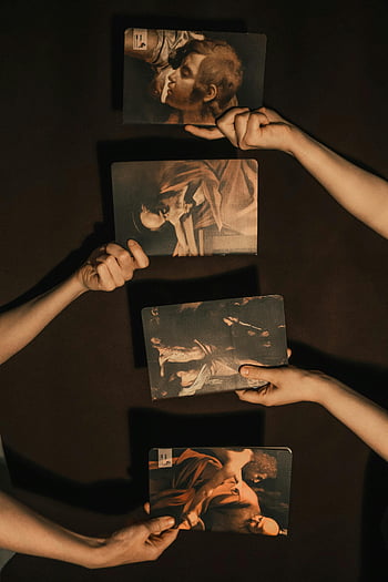 person holding photographs, art prints, classical paintings, dark backdrop, hands holding prints, four hands, classical art, art display, dark background, art collection, art prints collection