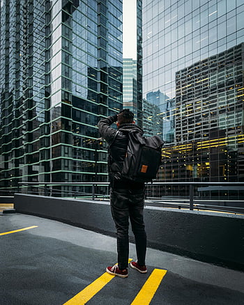 man with backpack, photographing skyscrapers, modern city setting, tall buildings, urban photography, cityscape, high-rise buildings, man standing, modern architecture, city life, urban scene
