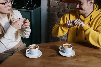 sign language, cafe, coffee cups, hand gestures, man and woman, communication, table, indoor, casual, yellow hoodie, white sweater