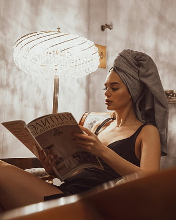 donna con asciugamano, rivista di lettura, illuminazione interna, luci soffuse, Avvolto nell'asciugamano, Lettura della rivista, donna rilassante, asciugamano sulla testa, Scena indoor, impostazione accogliente, lampadario