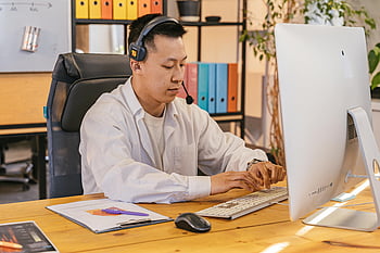 man in white shirt, using computer, businessman working, office desk, headset, focusing on tasks, computer monitor, keyboard, mouse, clipboard, office environment