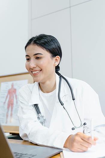 female doctor, white lab coat, stethoscope, smiling doctor, online consultation, laptop, confident doctor, medical professional, healthcare worker, telemedicine, virtual appointment
