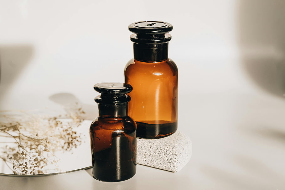 brown glass bottles, white surface, amber glass bottles, dried flowers, minimalist surface, aesthetic arrangement, decorative bottles, vintage bottles, glassware decor, still life photography, minimalist design