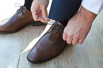 L'uomo che lega le scarpe, eleganti scarpe in pelle marrone, pavimento di legno, avvicinamento, uomo che indossa scarpe, scarpe formali, scarpe da sera, lacci delle scarpe, calzature da uomo, scarpe alla moda, moda maschile