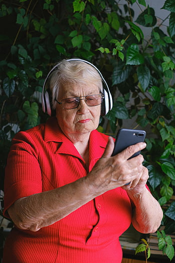 senior kvinde, hovedtelefoner, smartphone, nyder musik, indendørs, rød skjorte, ældre, Teknologibrug, afslappet omgivelse, grøn baggrund, afslappet atmosfære