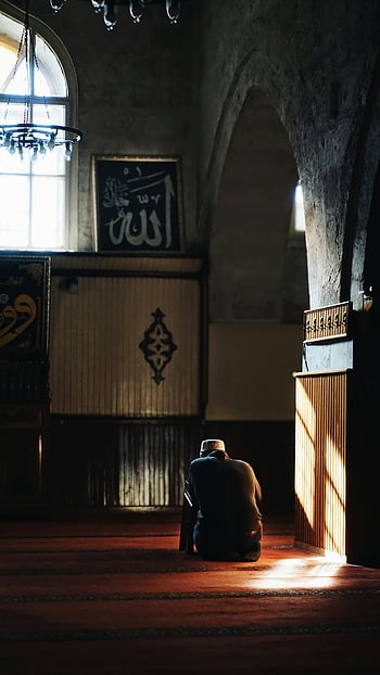 Muslimská modlitba, interiér mešity, spoře osvětlené, duchovní oddanost, klidná scéna, muž se modlí, islámské umění, lustr, oblouk, náboženské prostředí, modlitební čas
