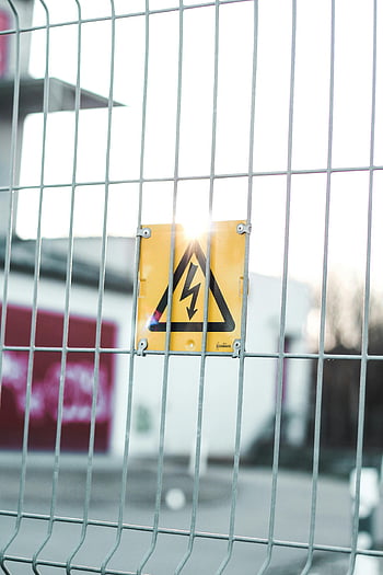 high voltage sign, metal fence, urban area, caution sign, safety warning, yellow sign, electrical hazard, warning symbol, industrial safety, caution symbol, urban safety