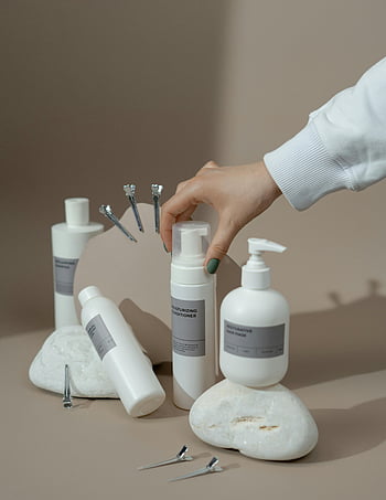 Sticle de piele, Sticle de plastic alb, Ajungând mâna, fundal bej, Afișare elegantă, balsam de hidratare, mască de păr, Configurare minimalistă, produse de infrumusetare, pietre albe, agrafe de par