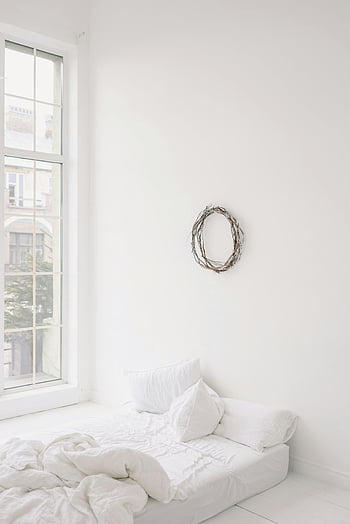 empty room, white bed, minimalist bedroom, large window, wall wreath, bright interior, white decor, modern bedroom, cozy space, simple design, natural light