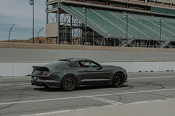 carro esportivo preto, pista de corrida vazia, arquibancadas, carro esportivo escuro, dirigindo, pista de corrida, faixa vazia, carro esportivo, estrada, carro