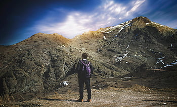 Muž stojící vedle hory, osamělý turista, fialový batoh, Robustní horský terén, živé nebe, venkovní dobrodružství, Mountain Exploration, scénické krajiny, turistika, fotografování přírody, cestovní fotografie