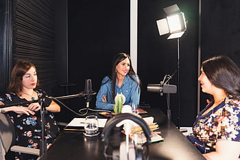 wanita duduk di meja, diskusi podcast, tiga wanita, Pengaturan dalam ruangan yang nyaman, Pemberdayaan, koneksi, mikrofon, Studio rekaman, percakapan kelompok, Peralatan Audio Profesional, Pengaturan pencahayaan