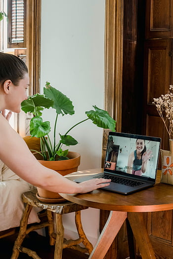 woman, online yoga class, video call, home, laptop, plant, wooden table, indoor, casual, smiling, virtual class