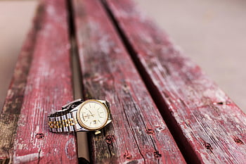 Round Gold-colored Analog Watch, elegant wristwatch, weathered red wooden bench, timekeeping style, gold watch, analog watch, red wooden bench, wristwatch display, gold-colored watch, elegant watch, wooden bench