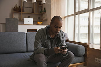 jonge etnische man, messaging, smartphone, comfortabele bank, Rustige binnenomgeving, huis, gefocust, man, telefoon gebruiken, woonkamer, casual kleding