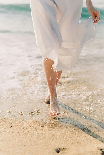female barefoot, walking on beach, white dress, sunlit beach, gentle ocean waves, beach scene, barefoot woman, beach walk, ocean waves, sandy beach, beach photography