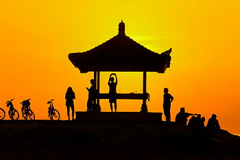sunset silhouette, people near gazebo, vibrant sunset, tranquil scene, silhouettes under gazebo, bikes in silhouette, outdoor scene, sunset backdrop, gazebo silhouette, people silhouettes, sunset tranquility
