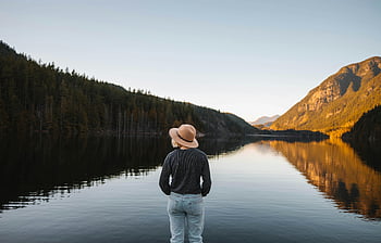 woman in hat, tranquil lake, mountain landscape, serene reflection, gray long sleeves, back view, standing by lake, peaceful scenery, natural beauty, outdoor scene, calm waters