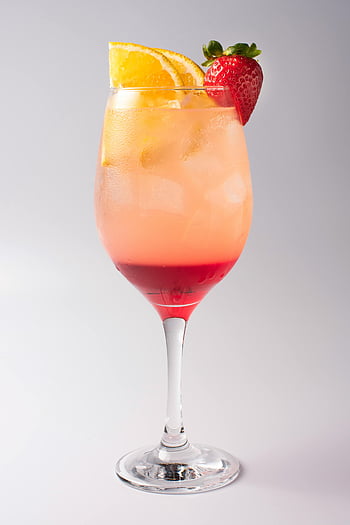 clear wine glass, red liquid, vibrant cocktail, strawberry garnish, orange garnish, summer drink, iced beverage, fruit cocktail, refreshing drink, wine glass cocktail, layered drink
