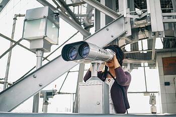 woman in purple cardigan, coin-operated binoculars, modern outdoor platform, woman using binoculars, outdoor observation, modern architecture, public viewing platform, coin binoculars, outdoor activity, woman observer, modern structure