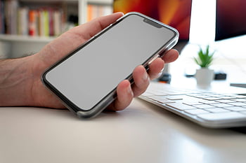 smartphone, modern technology, hand holding smartphone, smartphone with blank screen, desk setup, computer keyboard, workspace, indoor office setting, plant on desk, modern workspace, technological devices