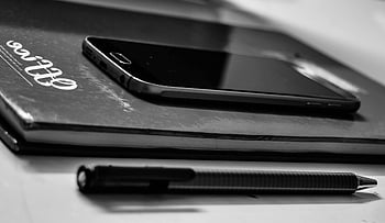 black Samsung Android smartphone, monochrome close-up, smartphone, notebook, pen, office desk, black and white, office supplies, desk setup, work tools, productivity items