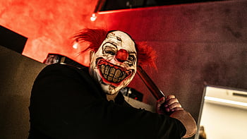 creepy clown, frightening mask, holding knife, indoors, red lighting, scary mask, person holding ax, horror scene, spooky atmosphere, clown horror, indoor horror setting