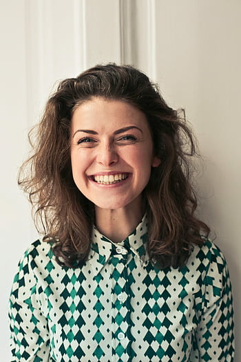 Frau im Kragenhemd, freudige Brünette, lebendiges Lächeln, Innenporträt, Glück, Positivität, lächelnde Frau, Innenfotografie, Lässiger Kleidungsstil, gemustertes Shirt, fröhlicher Ausdruck