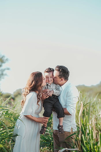 Par kysser son, familjens ögonblick, soligt landsbygdsfält, Kärlek och samhörighet, glad familj, utomhusfamiljfoto, Föräldrar som kysser barn, familj i naturen, landsbygdsfamiljescen, familjebindning