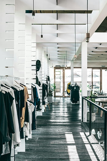 การตกแต่งภายในร้านค้าแฟชั่น, เสื้อผ้าบนชั้นวาง, ร้านขายเสื้อผ้าร่วมสมัย, เครื่องแต่งกายที่มีสไตล์, แสงธรรมชาติ, การออกแบบตกแต่งภายใน, ชั้นวางเสื้อผ้า, ร้านค้าสมัยใหม่, ค้าปลีกแฟชั่น, พื้นไม้, เสื้อผ้าที่แขวน