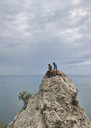Folk, der sidder på rock, stenet klippe, havudsigt, overskyet himmel, to personer, naturlandskab, udendørs eventyr, kystlandskab, naturskøn udsigt, rock formation