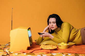 Vrouw in het geel shirt, tv kijken, Vintage televisie, ontspannend in bed, Snacking op chips, gele chips, gezellige setting, binnenscène, Casual levensstijl, retro sfeer, oranje achtergrond