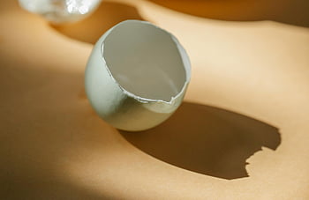 broken eggshell, white eggshell, sunlit surface, soft shadows, kitchen table, sunny morning, simplicity, fragility, close-up, eggshell fragment, natural light