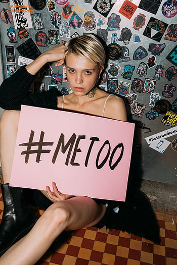 座っている女性、 床、 ピンクの紙のプラカード、 #MeTooサイン、 ステッカーで覆われた壁、 行動主義、 抗議、 社会運動、 エンパワーメント、 気づき、 男女平等