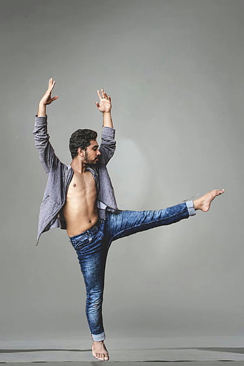 male dancer, mid-movement, flexibility, denim jeans, gray background, dance pose, artistic expression, studio shot, dynamic movement, barefoot dance, contemporary dance