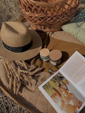 brown straw hat, glass jars, open book, picnic blanket, woven basket, autumn picnic, relaxing setup, outdoor scene, natural elements, picnic accessories, cozy atmosphere