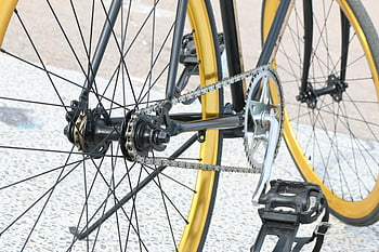 black bicycle, yellow rims, bicycle chain, gear system, urban setting, detailed view, bicycle components, bike parts, cycling equipment, street scene, bicycle wheels