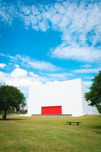 modern building, red door, lush greenery, clear blue sky, bright photo, park, white building, outdoor scene, architectural design, natural setting, sunny day