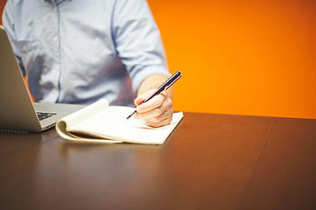 persona che scrive, Nota, computer portatile grigio, sfondo arancione vibrante, spazio di lavoro, scrivania, penna, taccuino, mano, ufficio, produttività